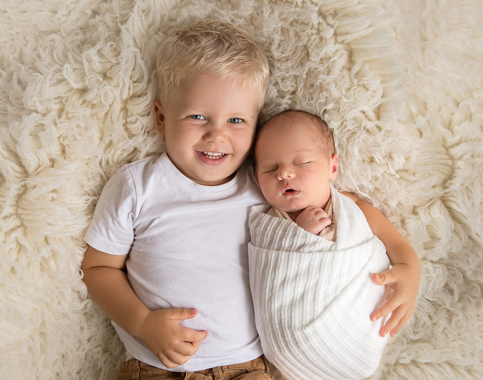 Blonde haired big brother with his newborn baby brother in a posed newborn session on the sunshine coast
